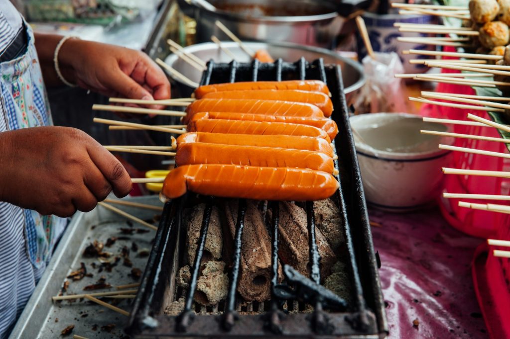 A street vendor makes grilled Thai sausages on skewers at the Warorot Market, Chiang Mai, Thailand.